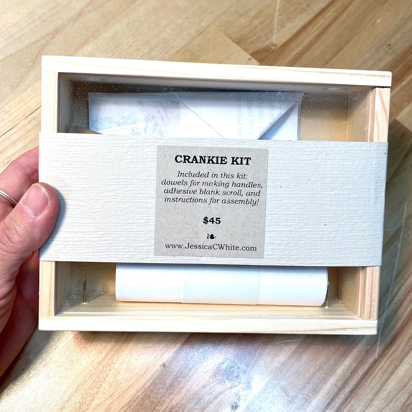Wooden box containing a crankie kit with a label on a wooden surface